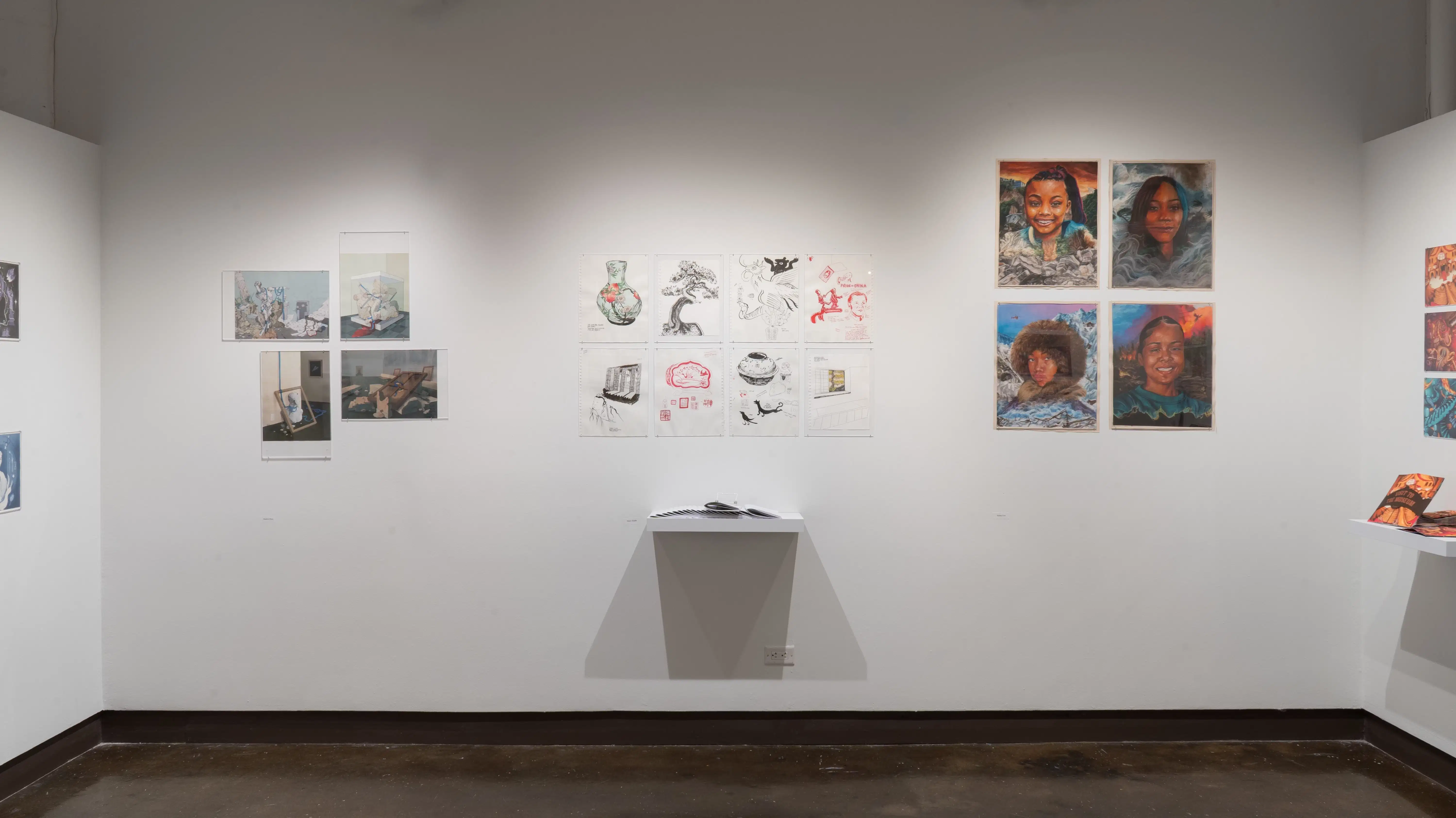 aIn the center of the gallery four alcove, two rows of simple illustrations are hung on the wall above a shelf holding many paper zines. To the right, four portraits hang in a grid, and to the left there are four illustrations of debris and objects.