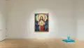 In a corner of the gallery, there is a sculpture of a blue fountain sitting on the ground. On the wall behind it, there is a very large painting of a saint-like person in a gold frame.