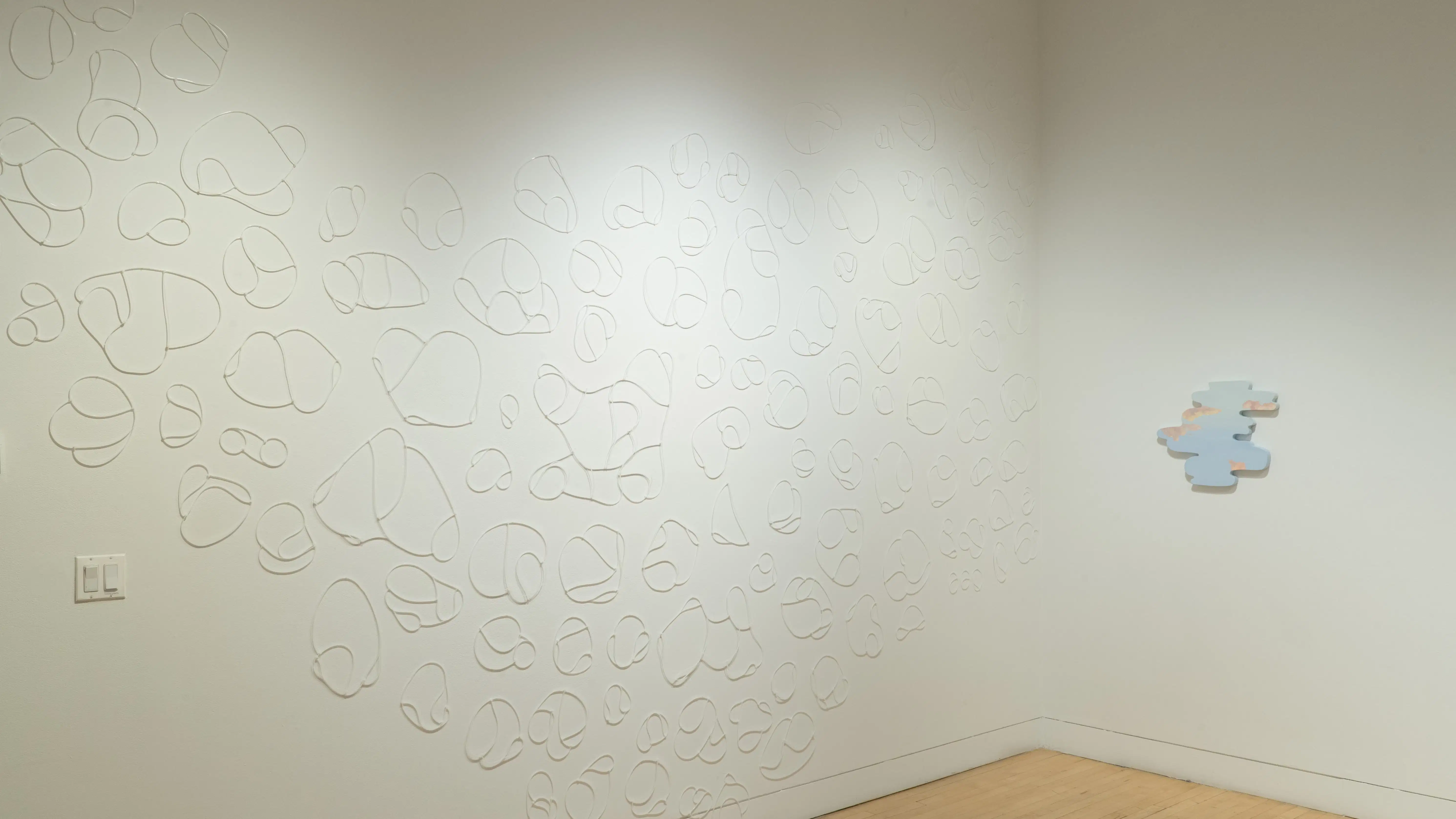 Inside the gallery, zip ties in organic shapes cover a wall. To the right, a pastel sky is painted on an organic-shaped panel.