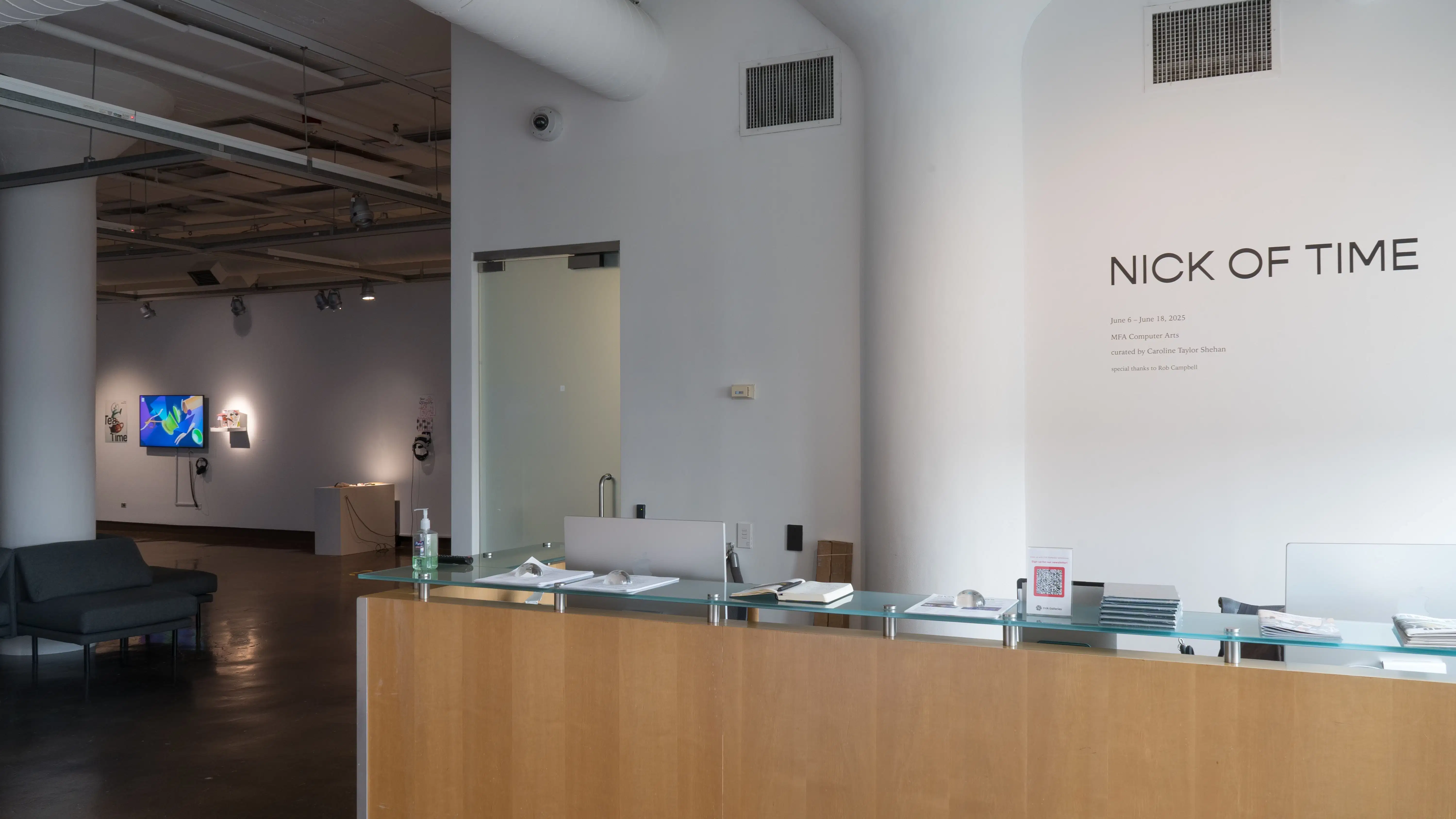 Wall vinyl above the front desk at the SVA Chelsea Gallery displays the title of the exhibition, “Nick of Time.” Works on monitors and pedestals are visible in the gallery past the desk.