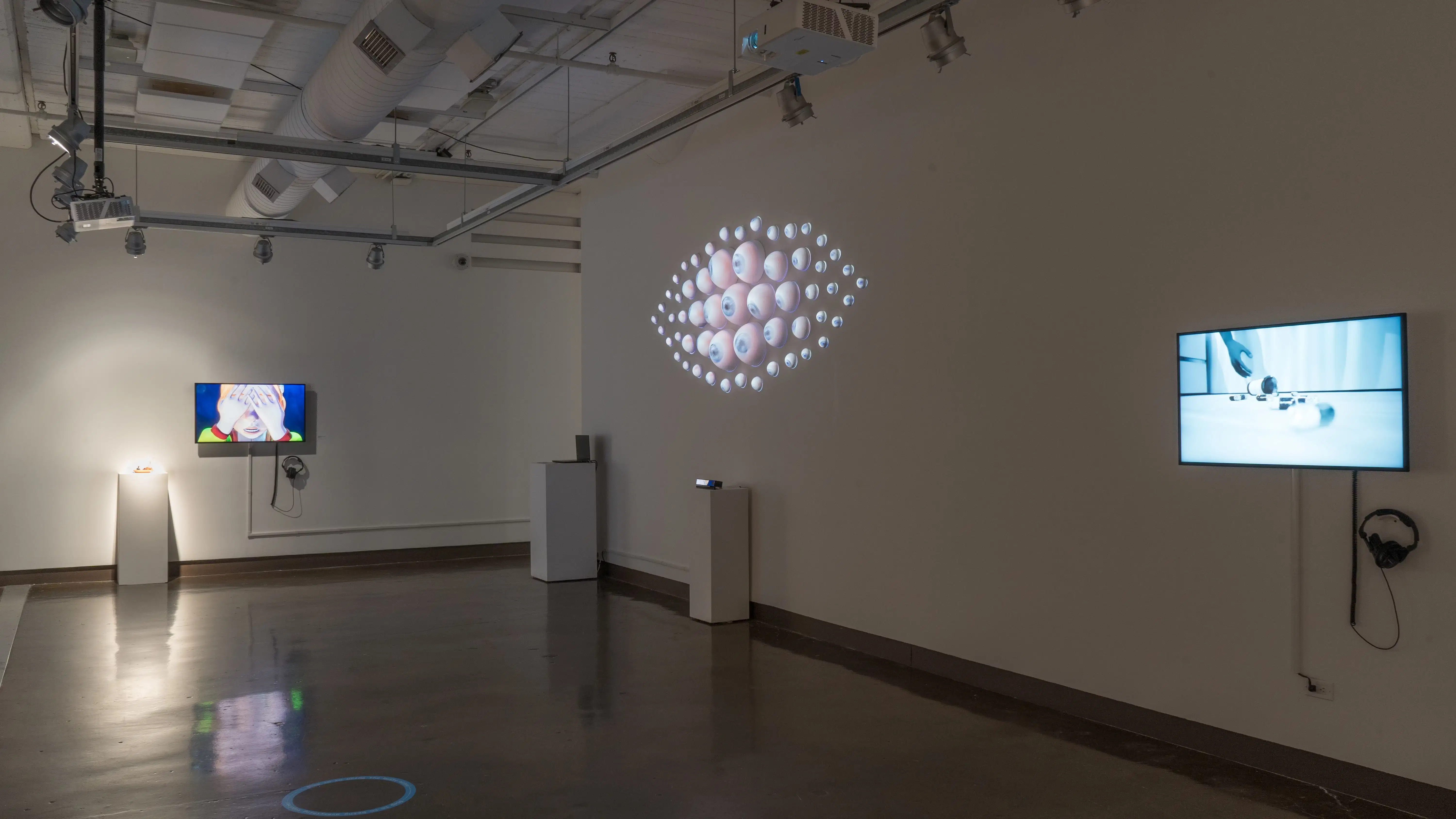 Many eyeballs of various sizes are arranged in an eye-like shape, protruding from the wall in gallery two. To the left and right of the eye, there are TV monitors playing animated videos.