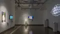 In gallery two, TV monitors hang on two of the three visible walls. On the third wall, many eyeballs of various sizes are arranged in an eye-like shape, protruding from the wall.