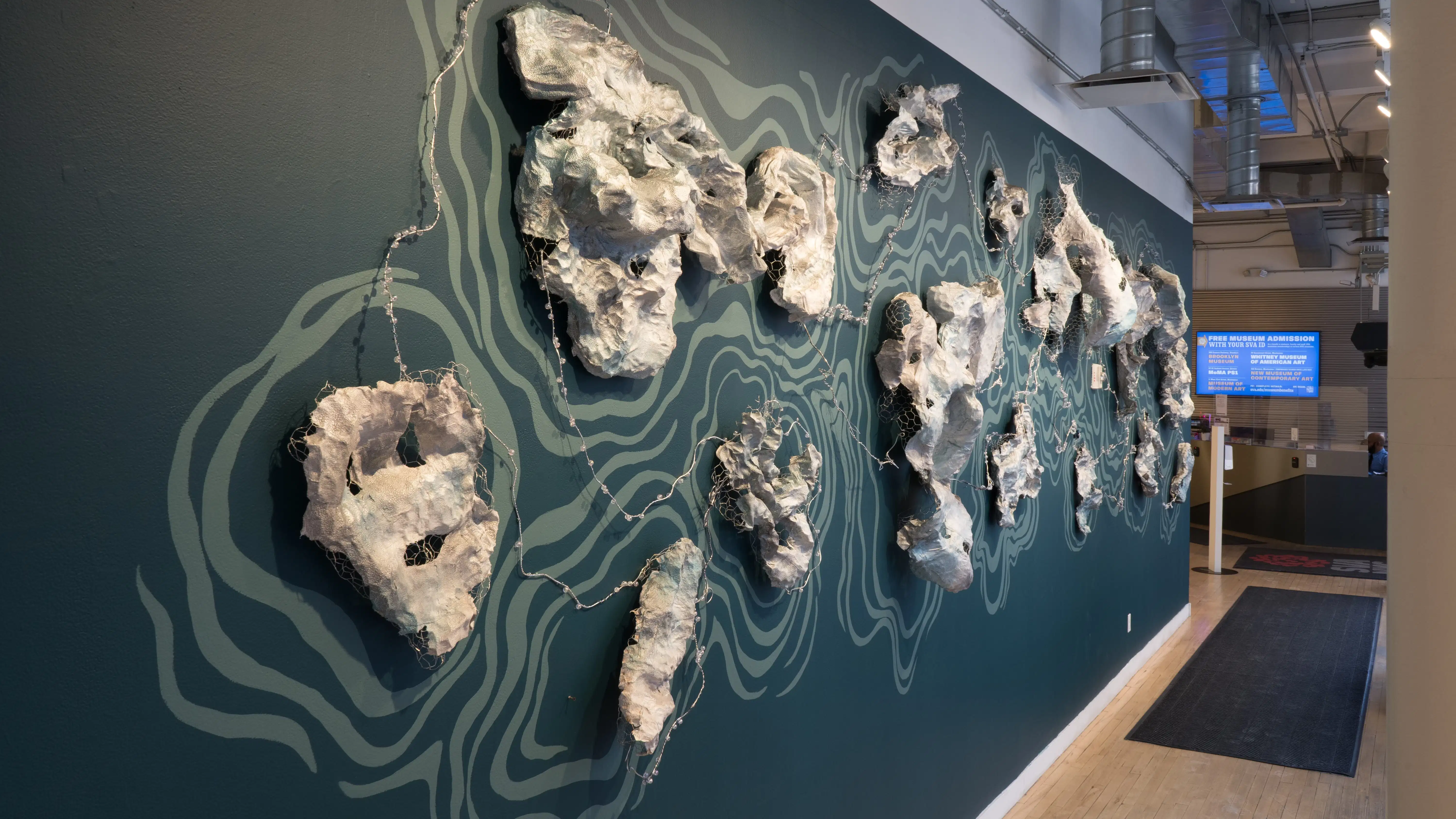 Angled view of the window wall at the SVA Flatiron Gallery facing east, showing a sculptural wall installation resembling sea creatures against a blue backdrop.