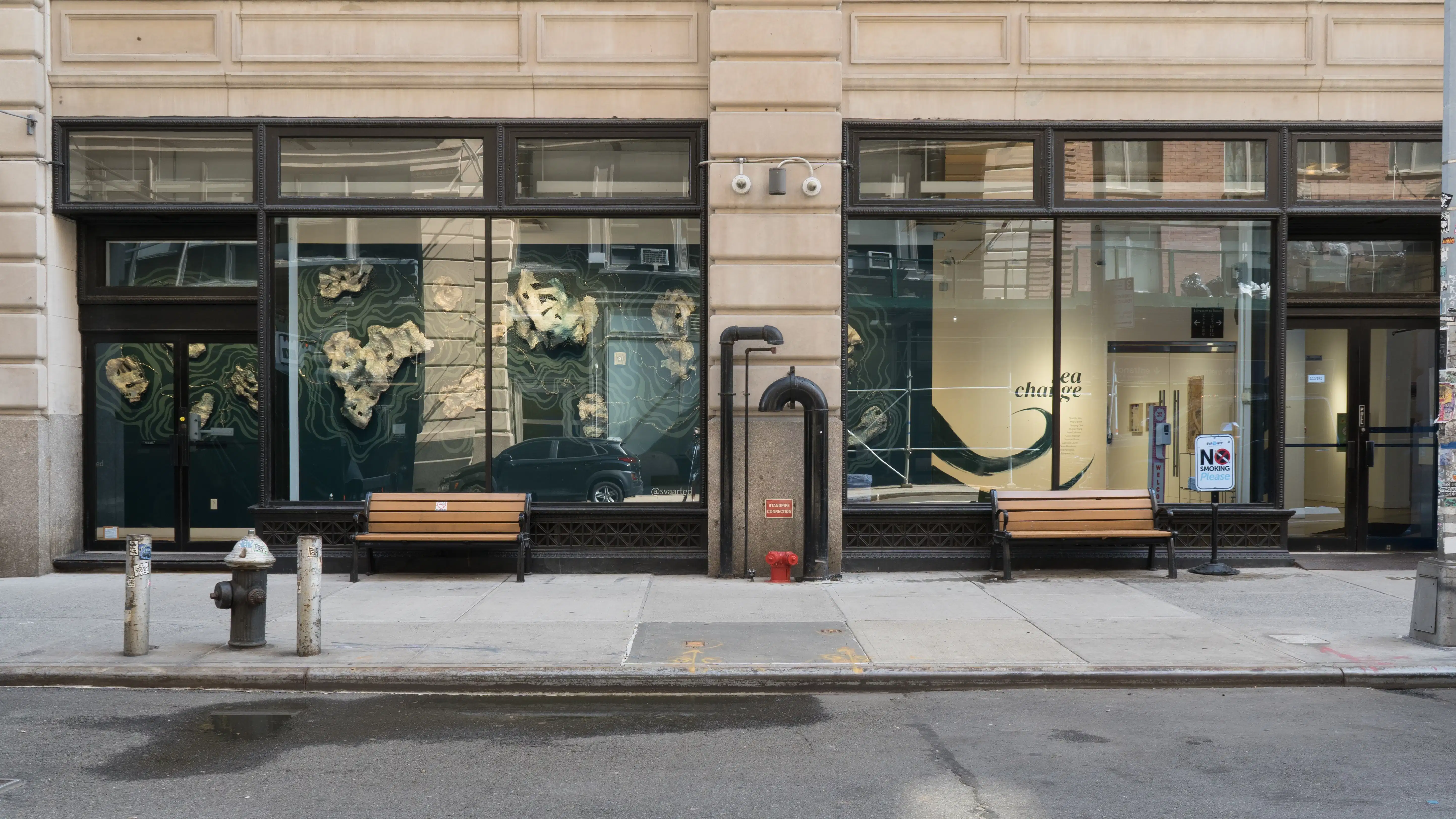 View from the street of the SVA Flatiron Gallery, showing a sculptural wall installation resembling sea creatures against a blue backdrop and the painted title wall in the background.