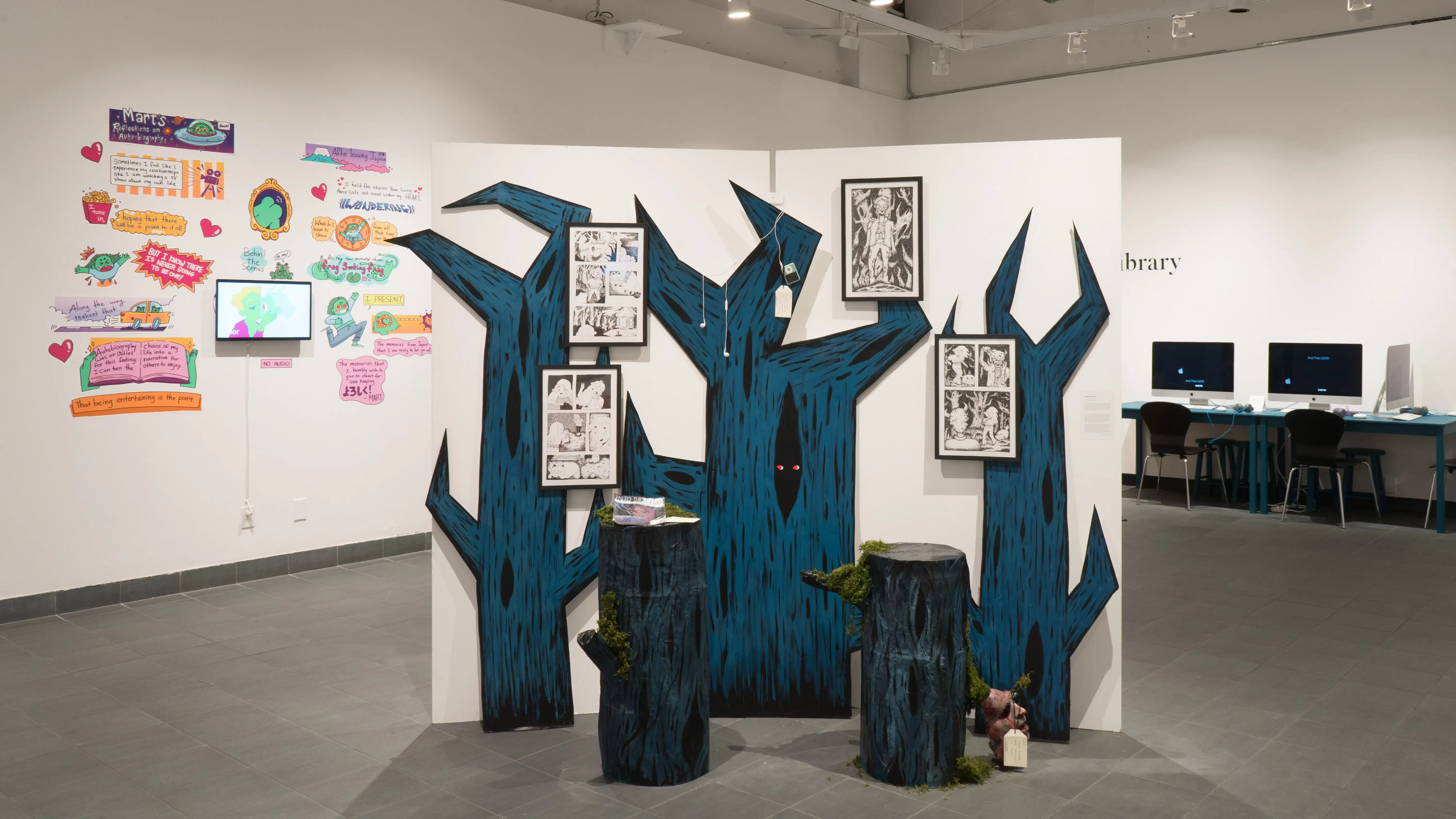 A divider in the middle of the room with cutouts of jagged, blue trees on top of it. Four frames of comics are on the trees, as well as an iPod and earphones. 