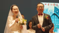 bride holds microphone next to groom, both have large smiles