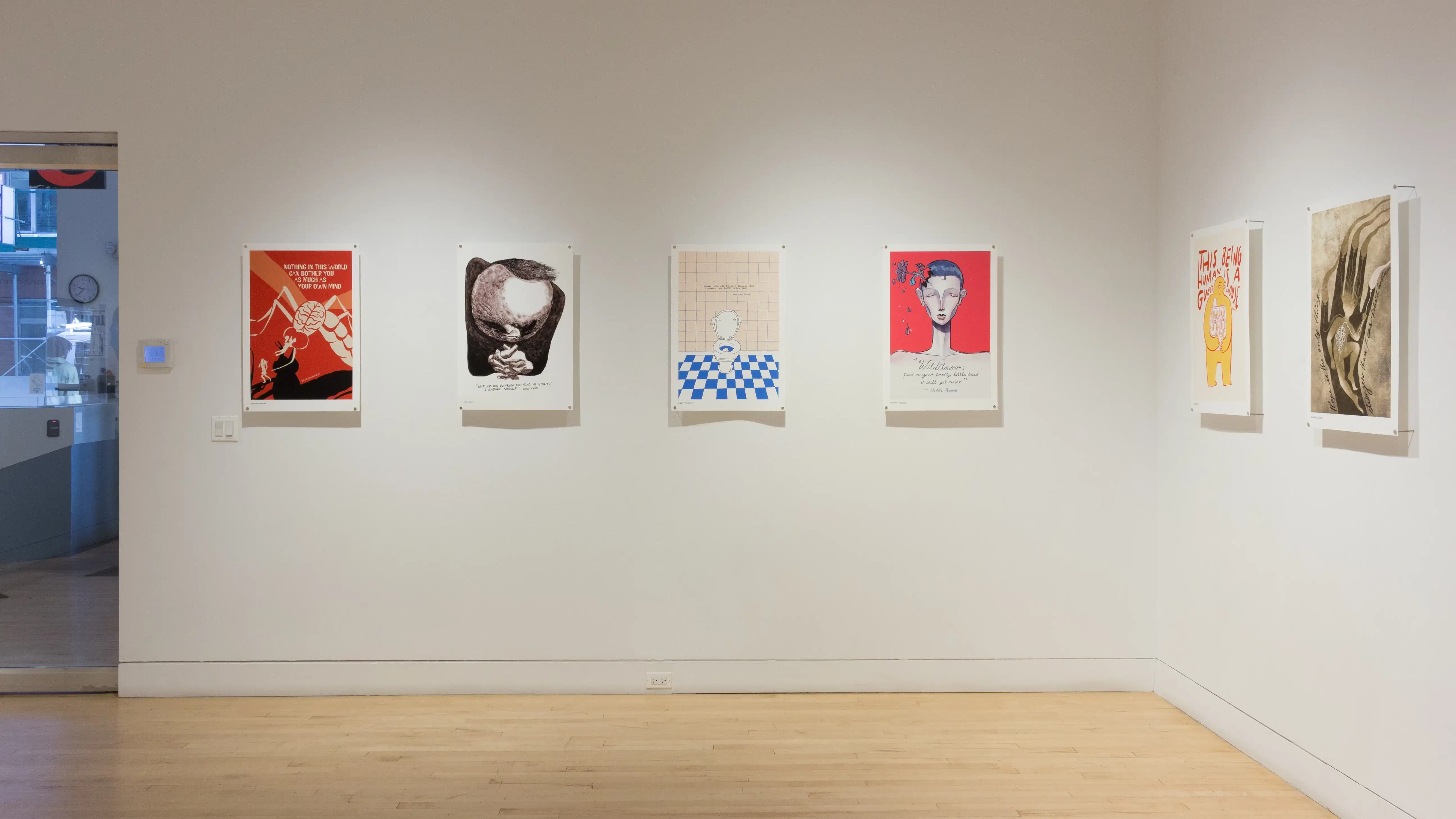 Six colorful poster illustrations in a row hang along the wall and a door to the entrance of the SVA Flatiron Gallery. 