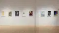 Eight poster illustrations hang in a row along the gallery wall. Some are in color and some in black and white.