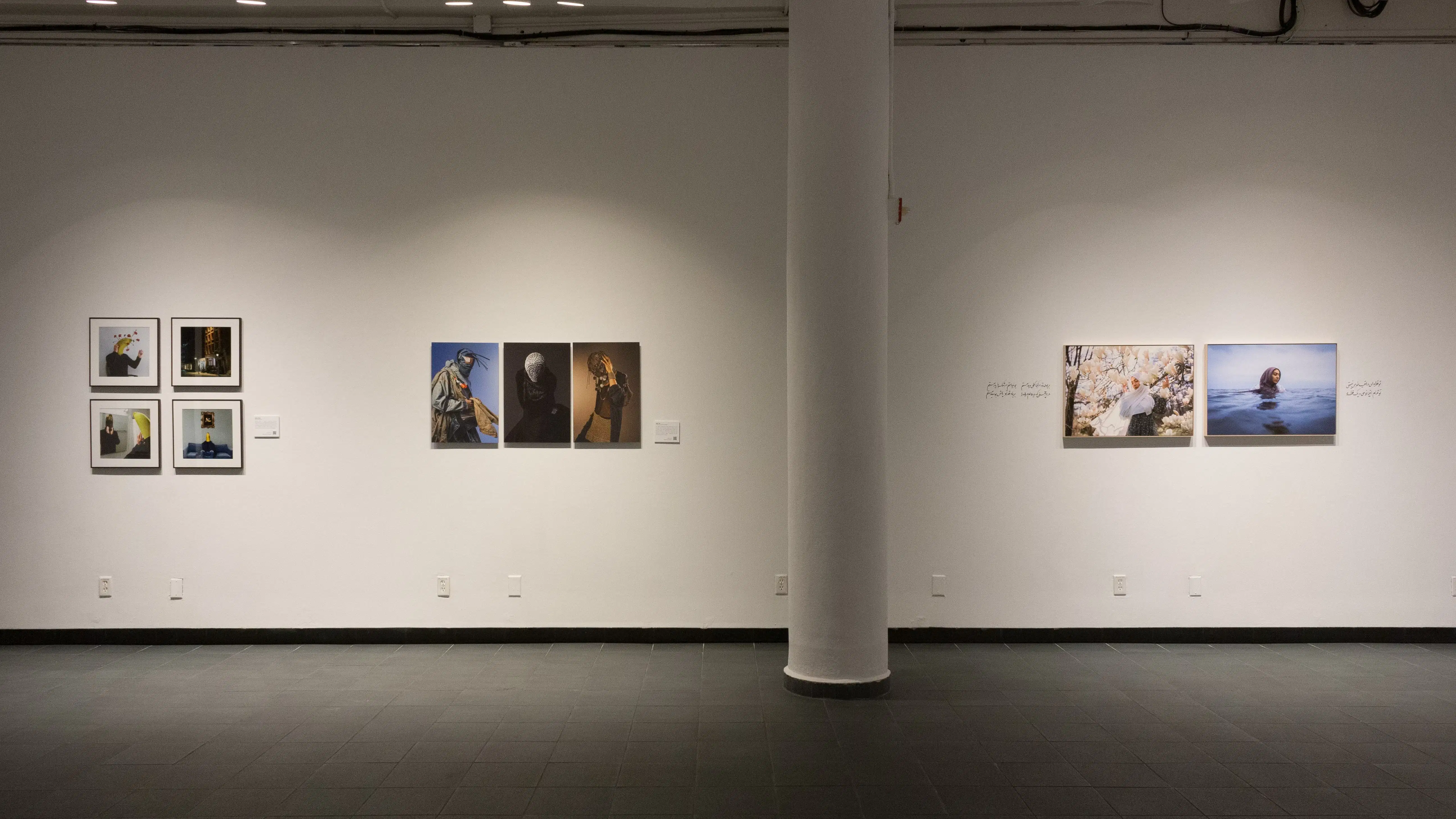 In the back gallery, three different photography projects hang on a wall in a row. The project furthest left features photos of a man with a banana for a head. The middle project shows people posing with their faces covered. The right project features a woman in a hijab posing in front of flowers and in the water.