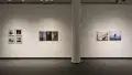 In the back gallery, three different photography projects hang on a wall in a row. The project furthest left features photos of a man with a banana for a head. The middle project shows people posing with their faces covered. The right project features a woman in a hijab posing in front of flowers and in the water.