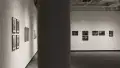 A series of black and white photographs hang on the back wall of the gallery.