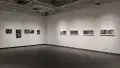 A series of black and white photographs hang on the back wall of the gallery. On the adjacent wall there are a row of diptych photographs.