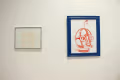 Installation shot of two framed pieces, the one on the left a drawing or nude bodies and the one of the right a print of a leather mask.
