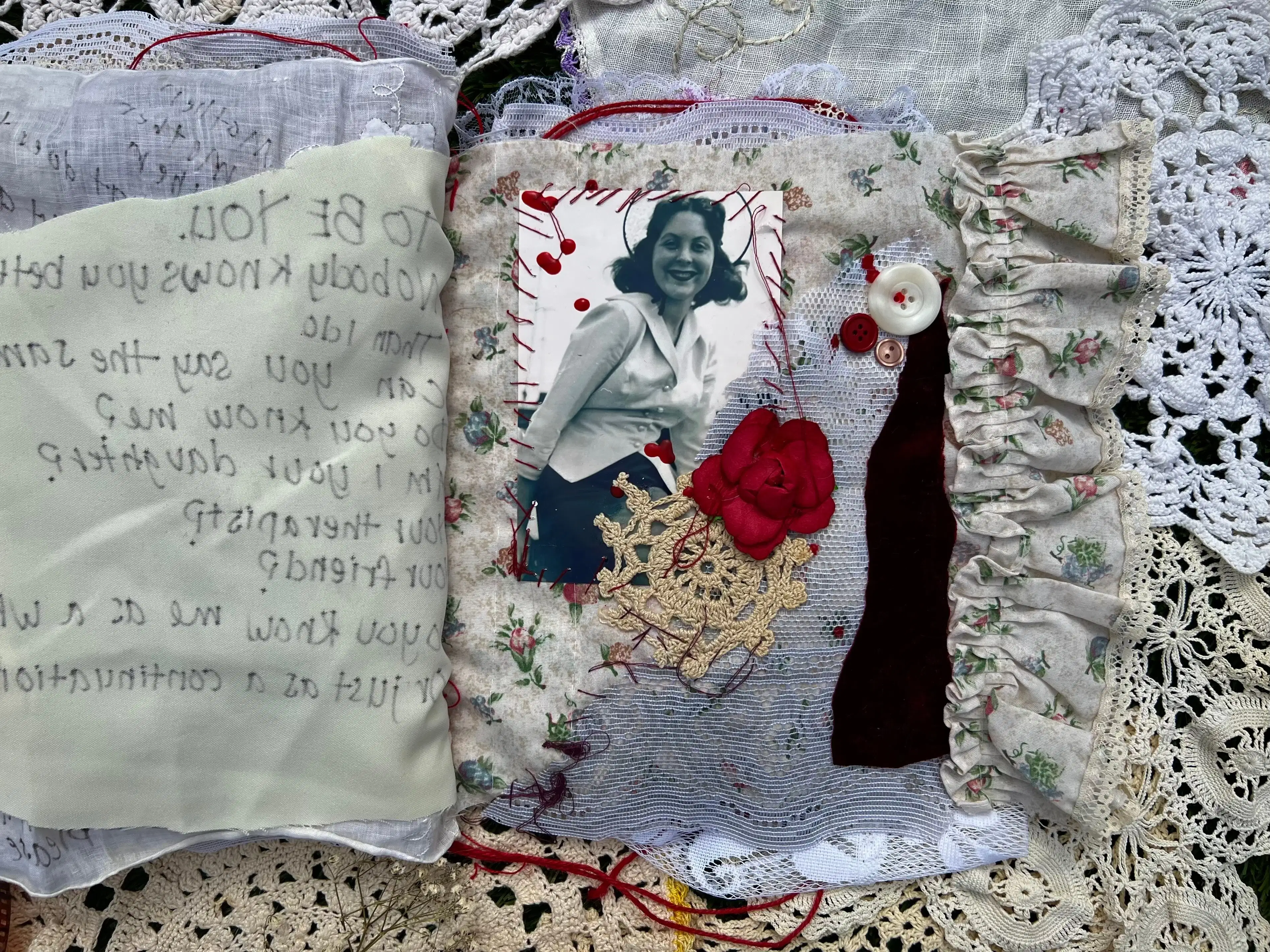 Page 15. The left page consists of 2 pieces of light fabric. Handwritten can be seen through the back side of this page. The right side consists of a delicate flower pattern with a stitched photograph of a woman smiling at the viewer. She is wearing white suit top over a dark skirt. To the right of the photograph and in the middle of the page is a red rose head on top of lace with three buttons towards the upper right or the lace holding a strip of velvet. 