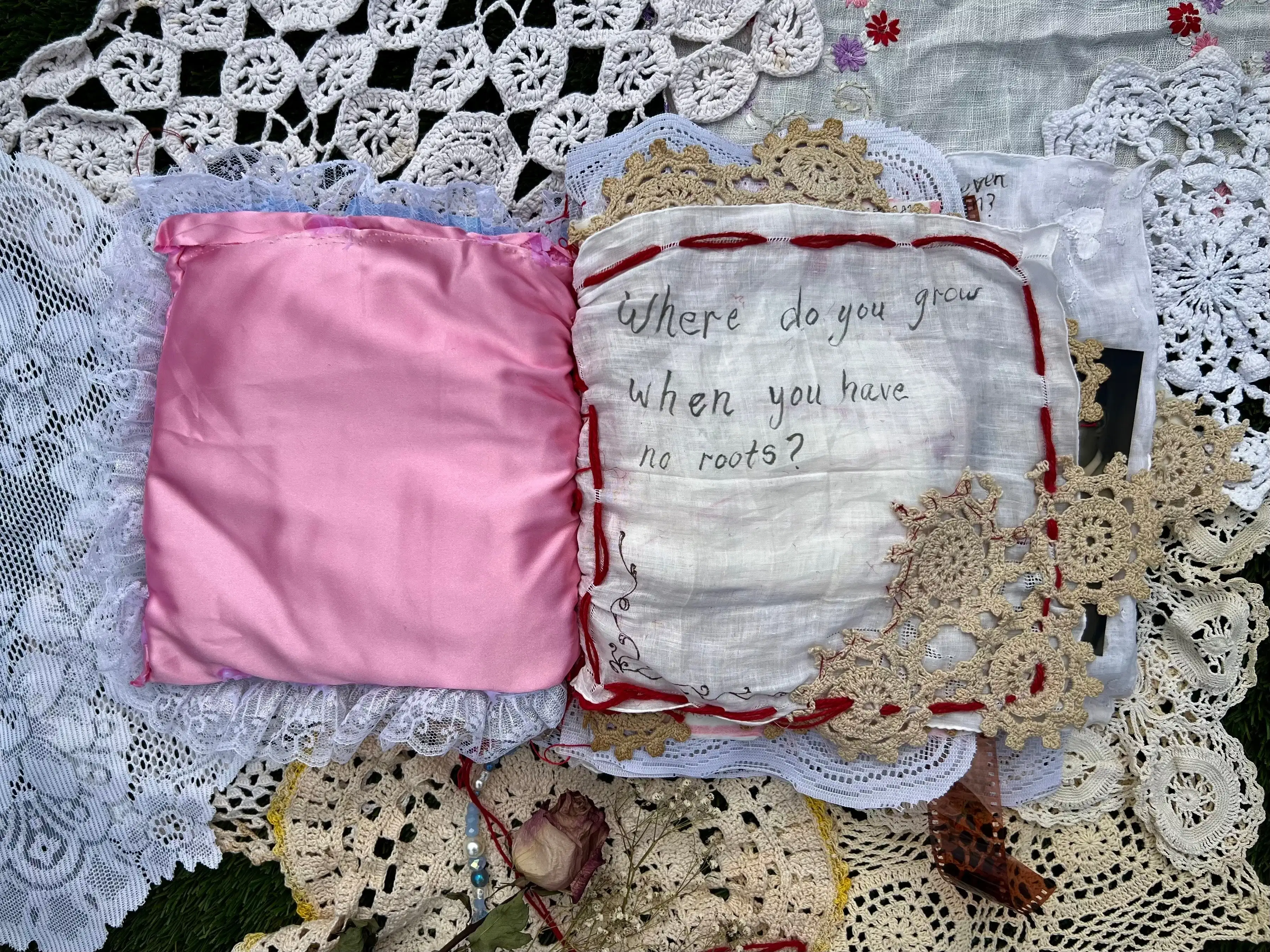 page 1. Pink satin cover is open to the left. On the right is white linen page framed in thick red wide stitching. Off-white lace is place on the bottom right-hand corner and stitched with thin thread. The film strip is still seen underneath the right page.