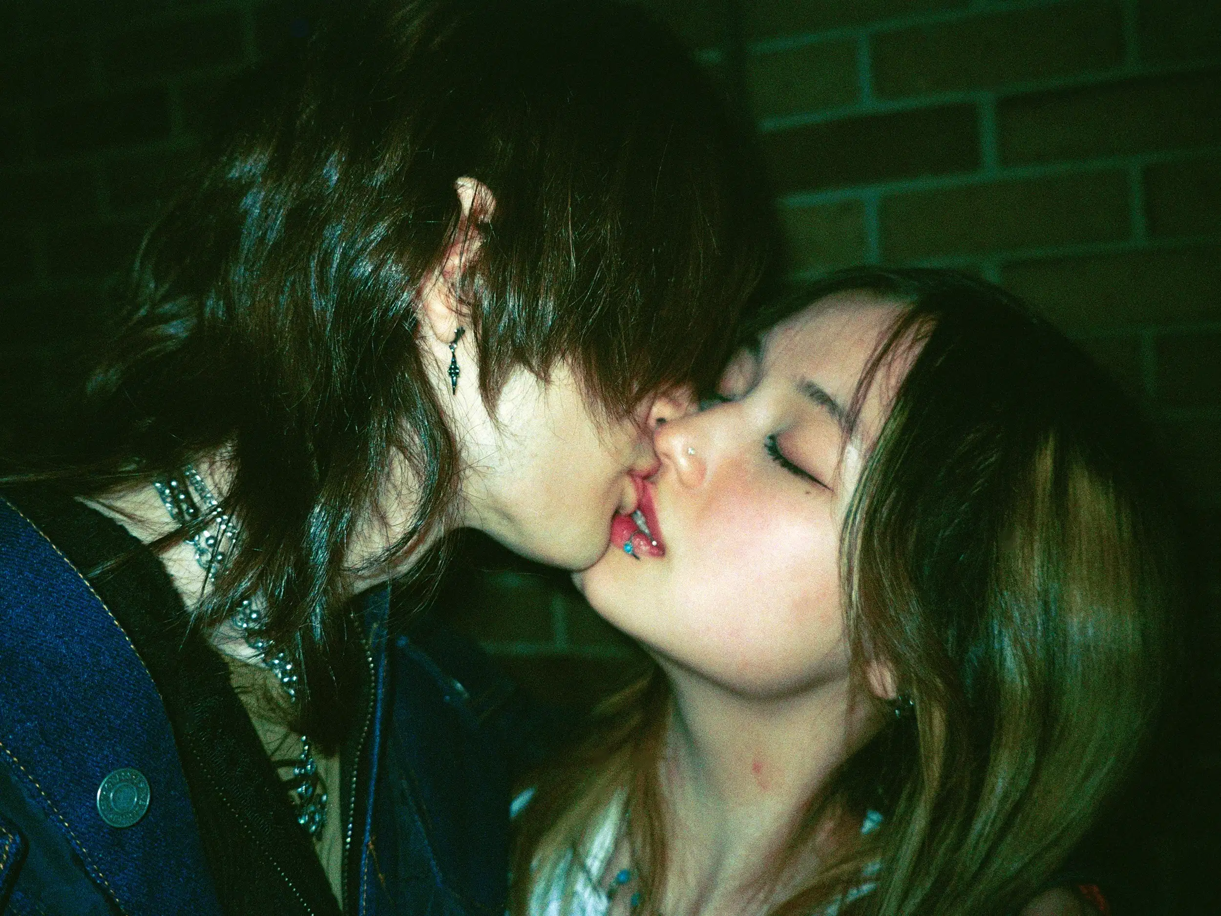 Two people kissing in front of a brick wall