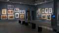 Back gallery space of the Visual Arts Museum, with framed photographs hung in salon style across two walls, with three minimalist black benches in the middle of the space.