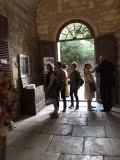 People gather at the entrance of the Romanesque cloister of Saint-Paul de Mausole. The floors and walls are made of stone, and natural light pours through the doorway.