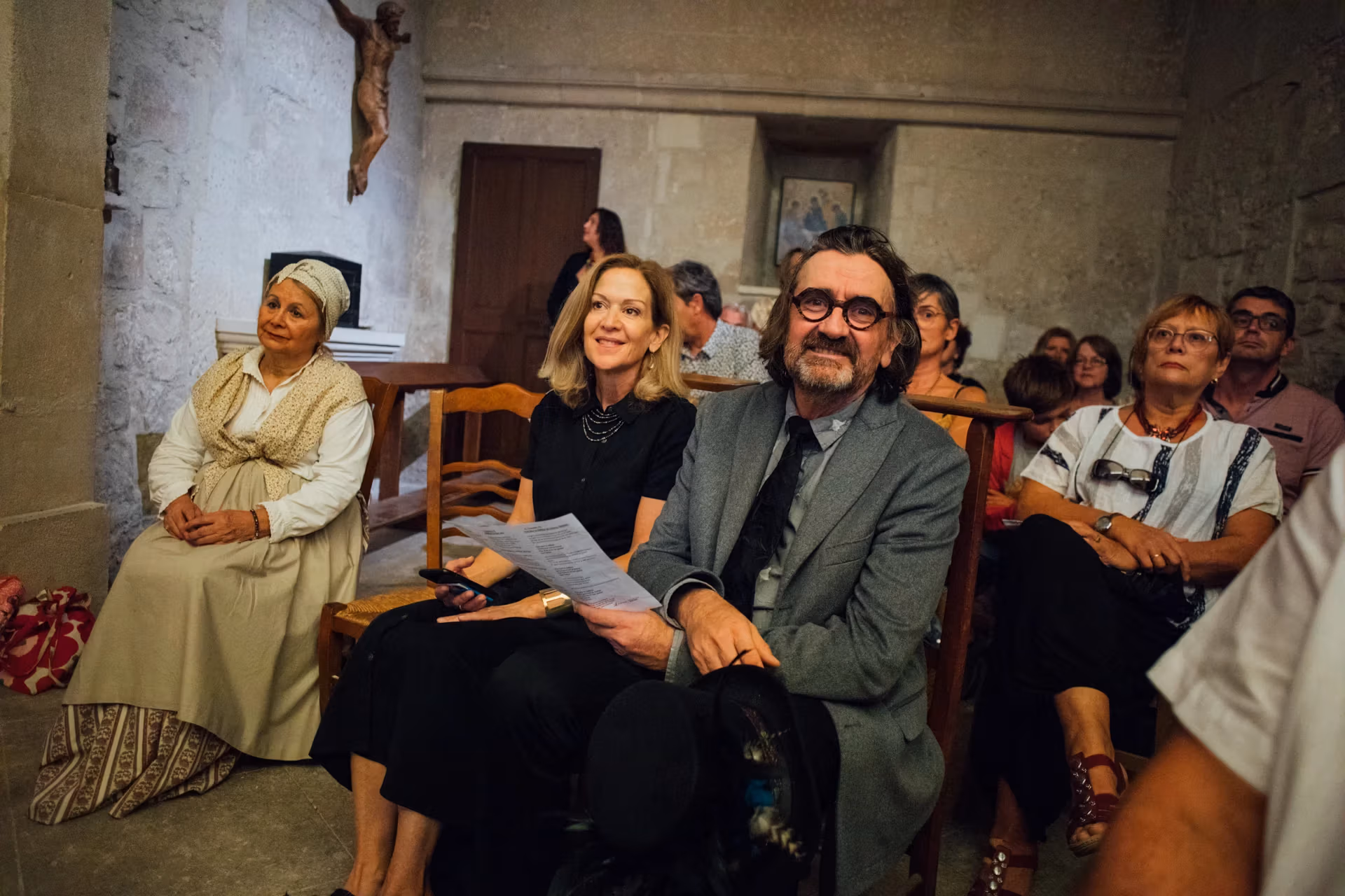 The same man sits among the crowd, looking toward the camera and the stage.