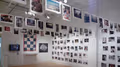 A gallery full of photographs. There is a quilt on the far wall.