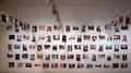 A wall of polaroid photos hung on wire. There are three rows of photos hanging in the air.