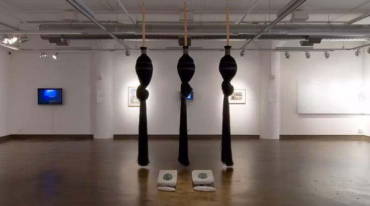 Three black sheets hang from the ceiling in an art gallery.