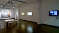 A large white room with a dining table on the floor, a TV on one wall and art work on the others.