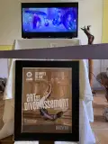 A monitor plays animations, and below the monitor, a framed poster reading "Art et Divertissement" or "Art and Revelry" sits on blocks.