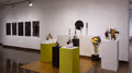 To the right are multiple modernist sculptures in geometric shapes, presented on pedestals or hung from the wall, and to the left are five minimalist black paintings on fabric hung from two nails each.