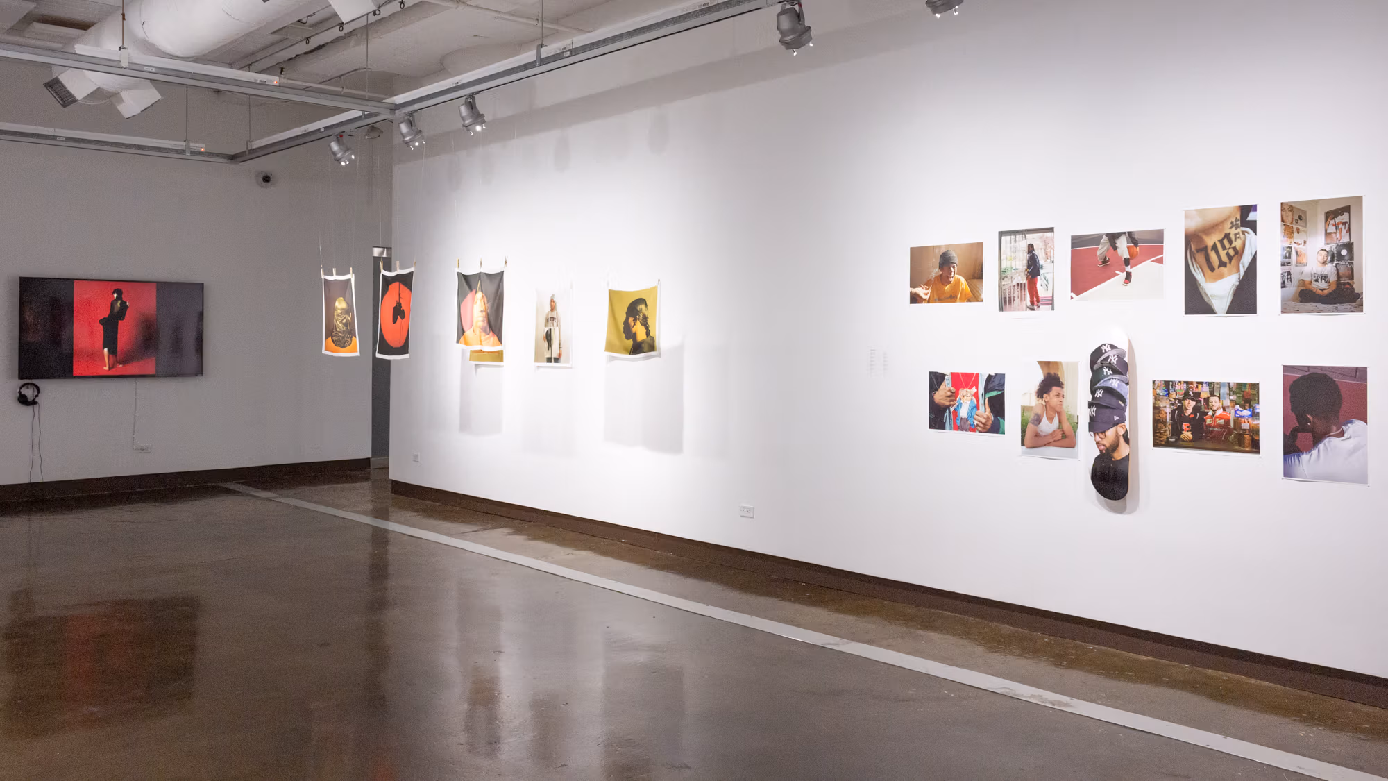 On the left is a monitor with an image of a woman standing in front of a red seamless background, to its right are six photographs printed on fabric, three of which are suspended and approximately 24 inches from those on the wall. On the far right is a six-by-two grid of photographic prints, the bottom center of which is printed on a skateboard.