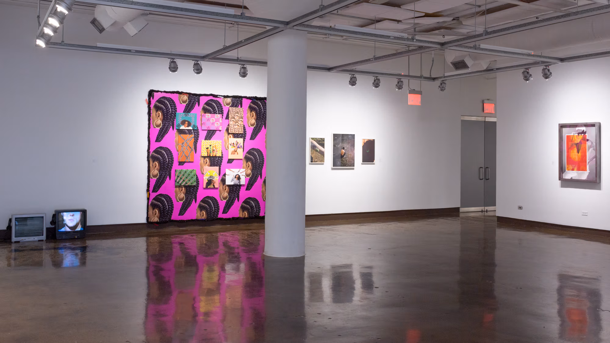 Installation shot of front gallery space at SVA Chelsea Gallery, showing two small television screens on the lower right, an installation piece in bright colors to its right, three framed images next to it, and on the far right is another wall with a framed gray and red artwork.