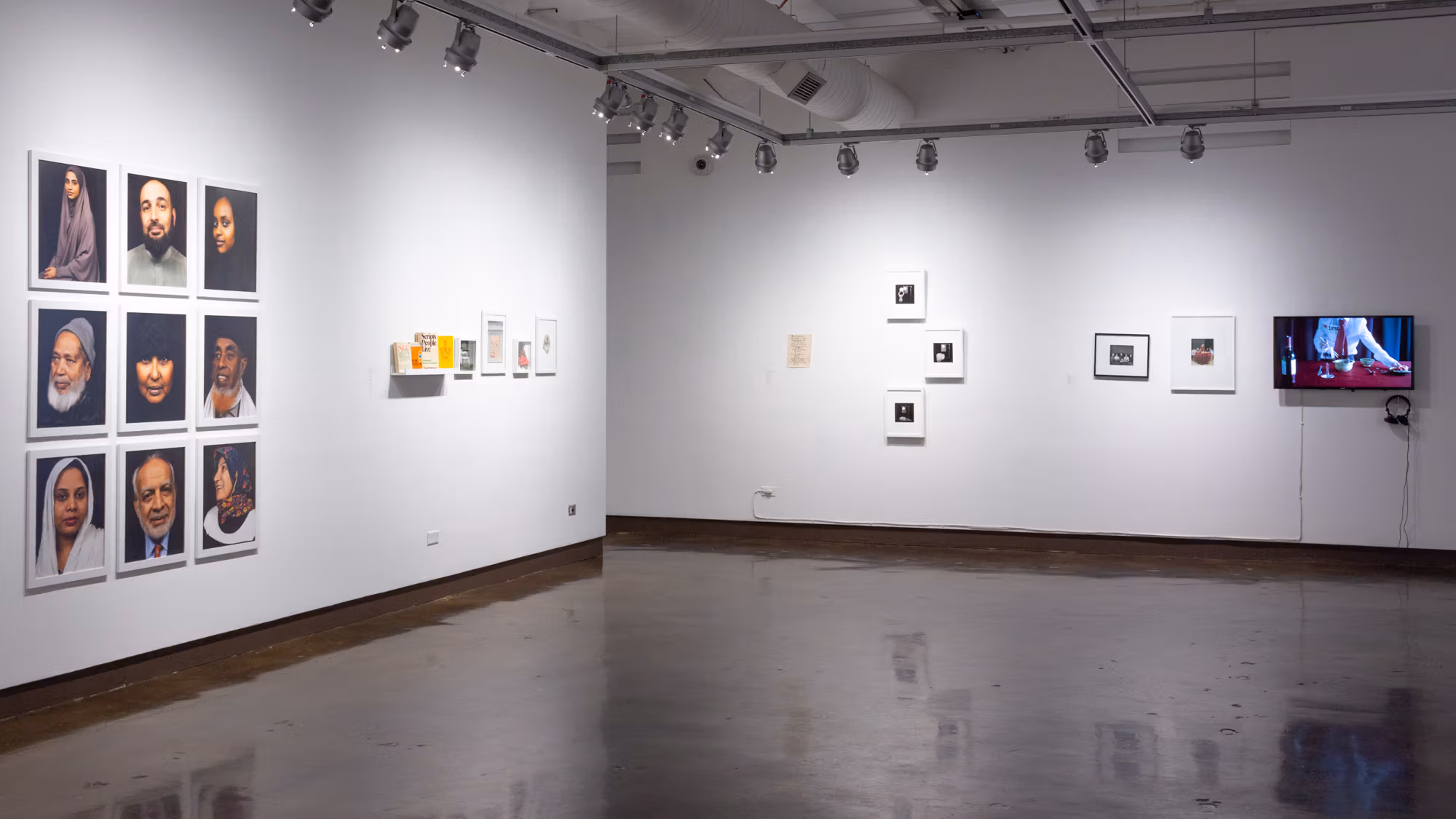 Photographic artwork installed on two different walls, with a three-by-three grid of portraits to the left, a row of appropriation-based pieces to its right, and on the second wall are five framed artworks and a monitor displaying a video of a person eating.