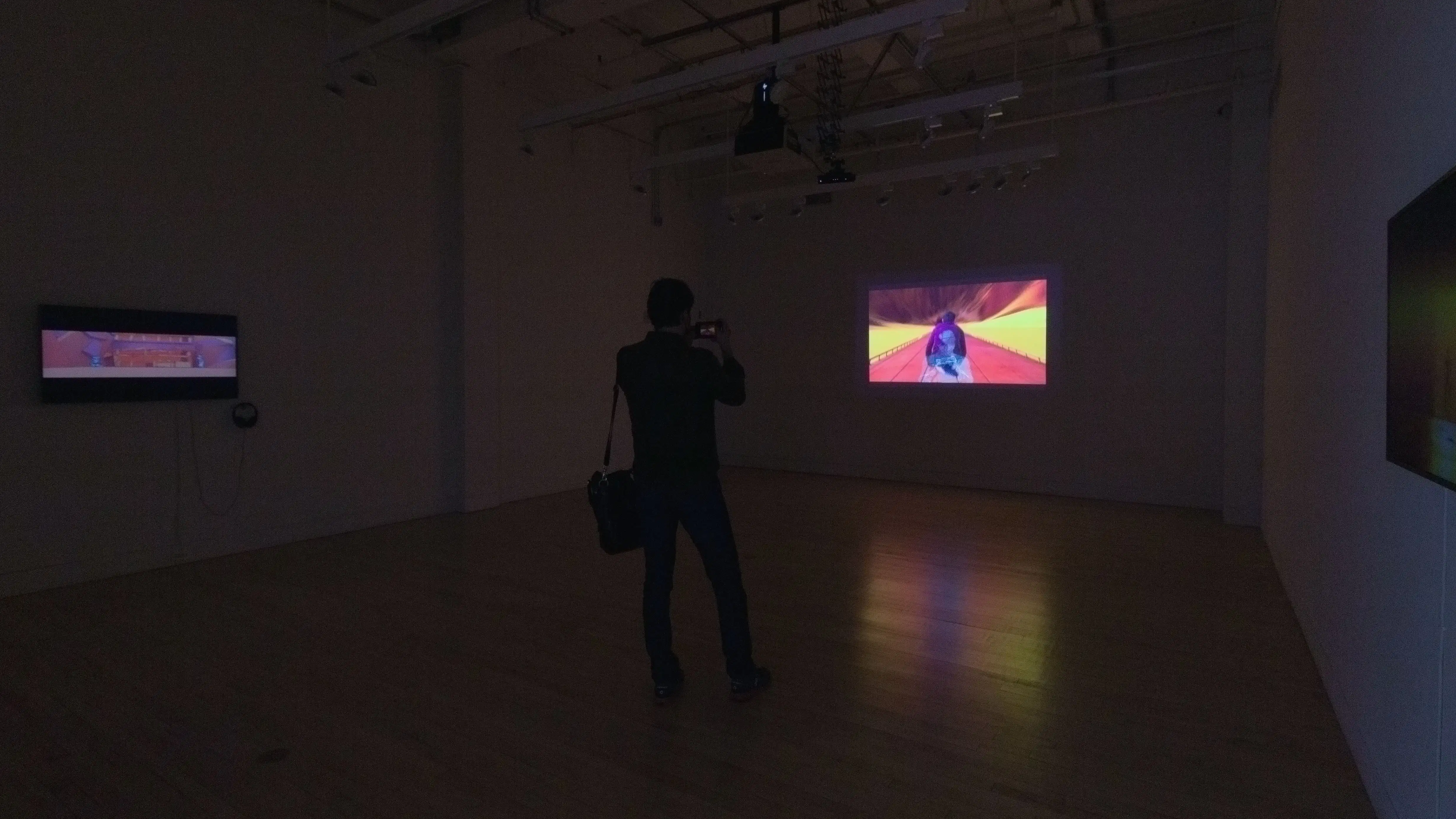 Multiple views of SVA Flatiron Gallery. There are three monitors playing various videos on the wall and an interactive projection. 