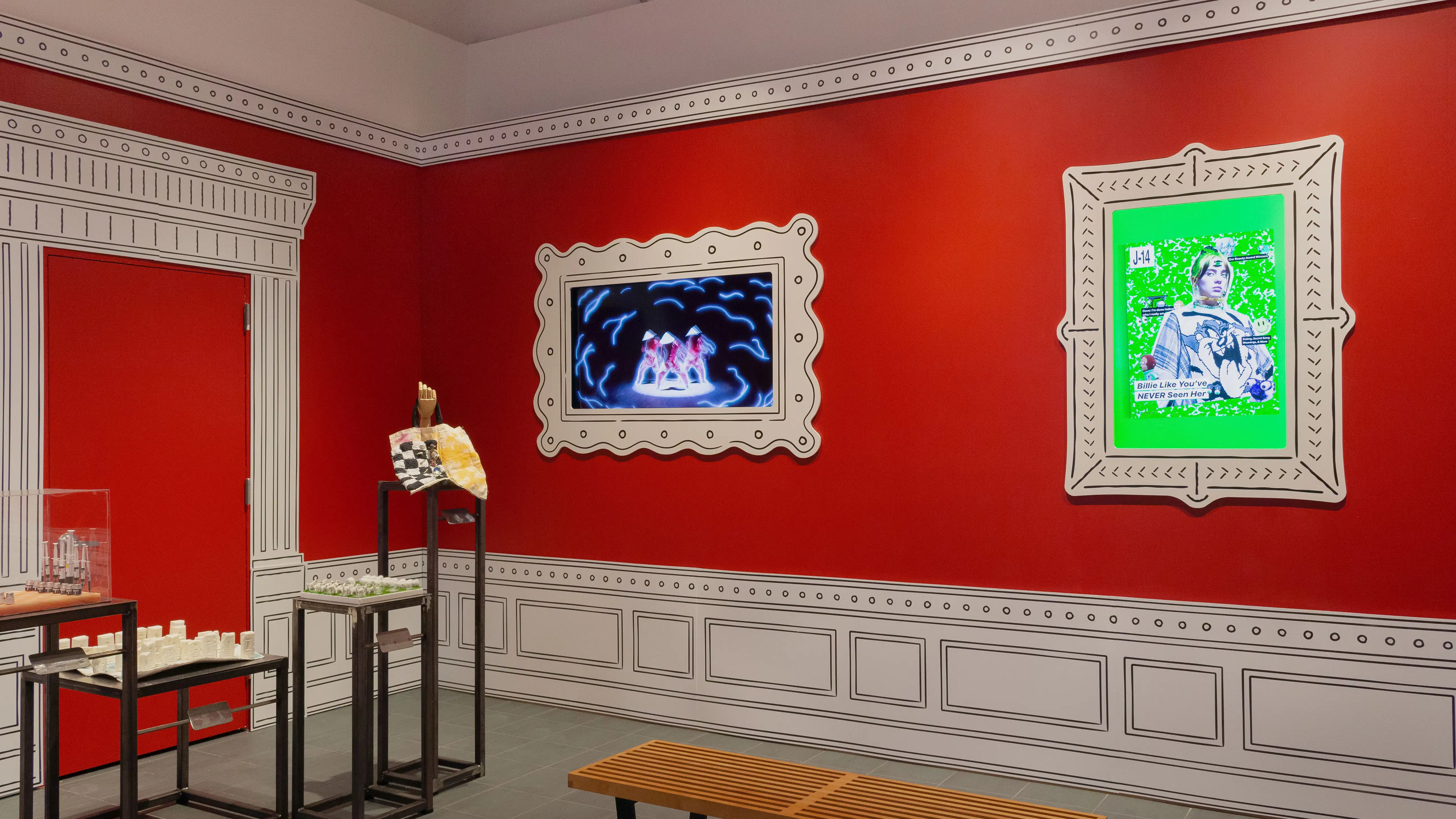 Multiple views of SVA Gramercy Gallery. The lobby is pained red with "Spring Salon" in ornate lettering and the gallery is painted blue. There are monitors in ornate frames playing student work through the gallery. In the center of the lobby and gallery are metal pedestals with student work on them. 