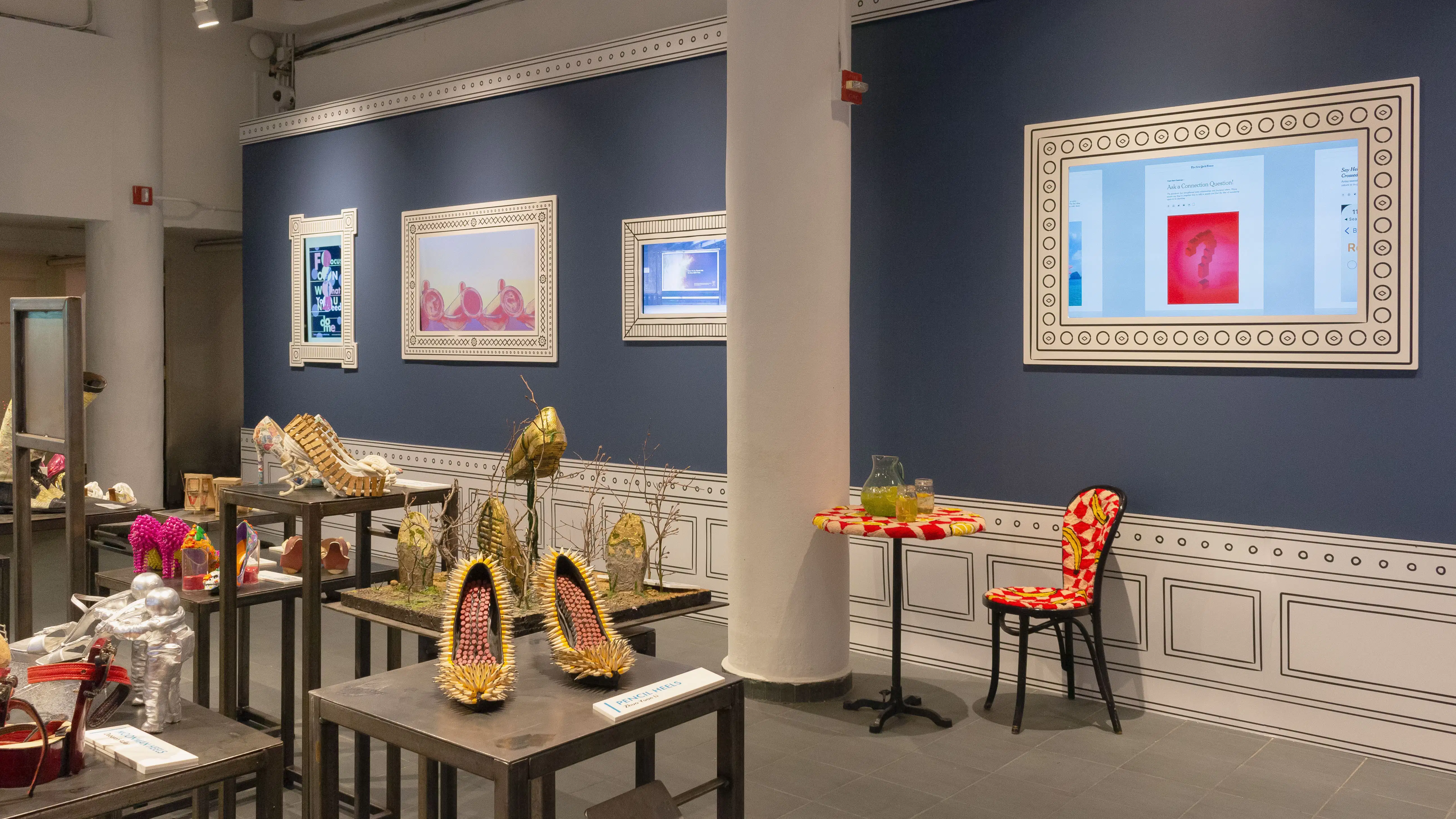 Multiple views of SVA Gramercy Gallery. The lobby is pained red with "Spring Salon" in ornate lettering and the gallery is painted blue. There are monitors in ornate frames playing student work through the gallery. In the center of the lobby and gallery are metal pedestals with student work on them. 