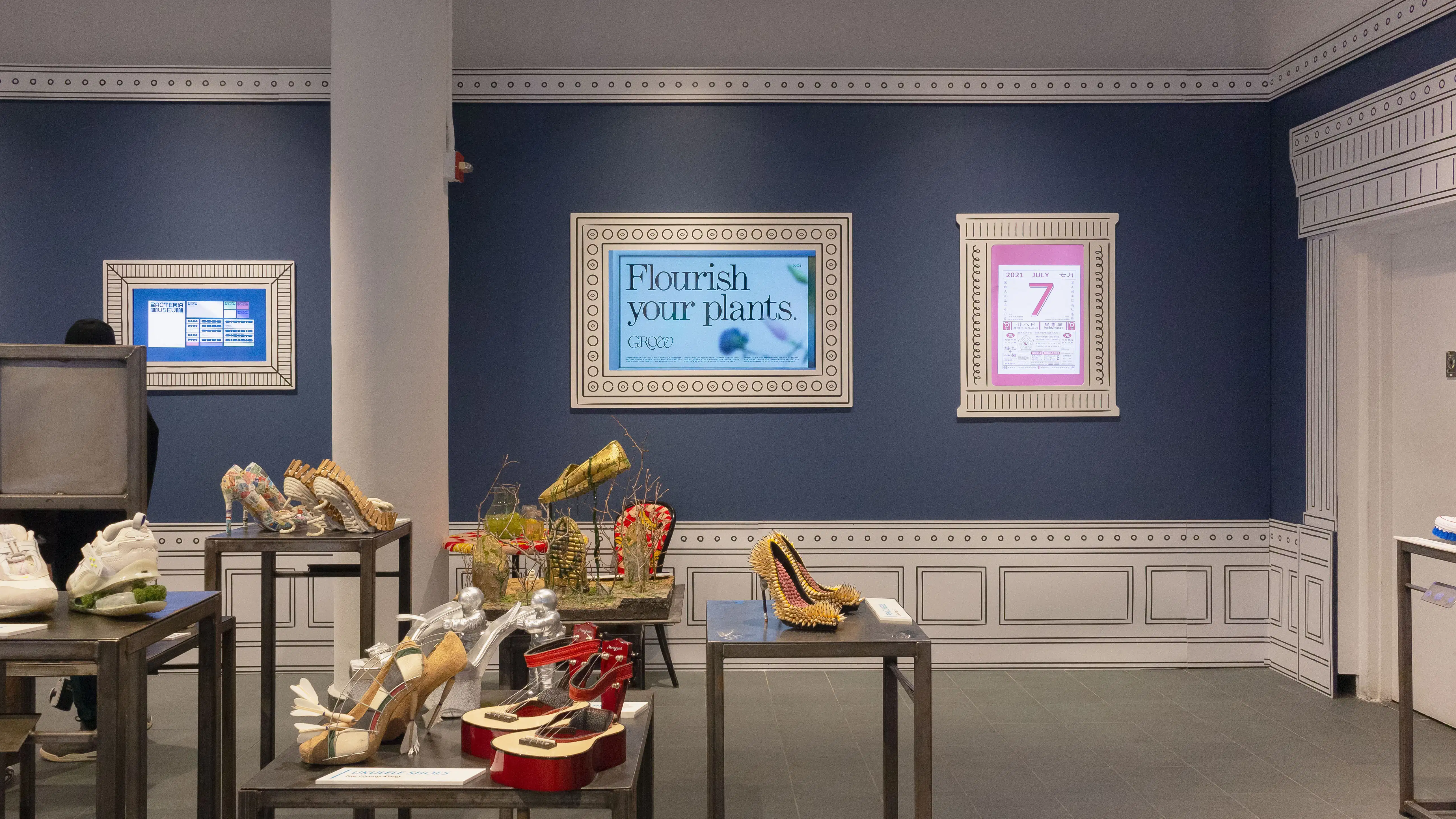 Multiple views of SVA Gramercy Gallery. The lobby is pained red with "Spring Salon" in ornate lettering and the gallery is painted blue. There are monitors in ornate frames playing student work through the gallery. In the center of the lobby and gallery are metal pedestals with student work on them. 