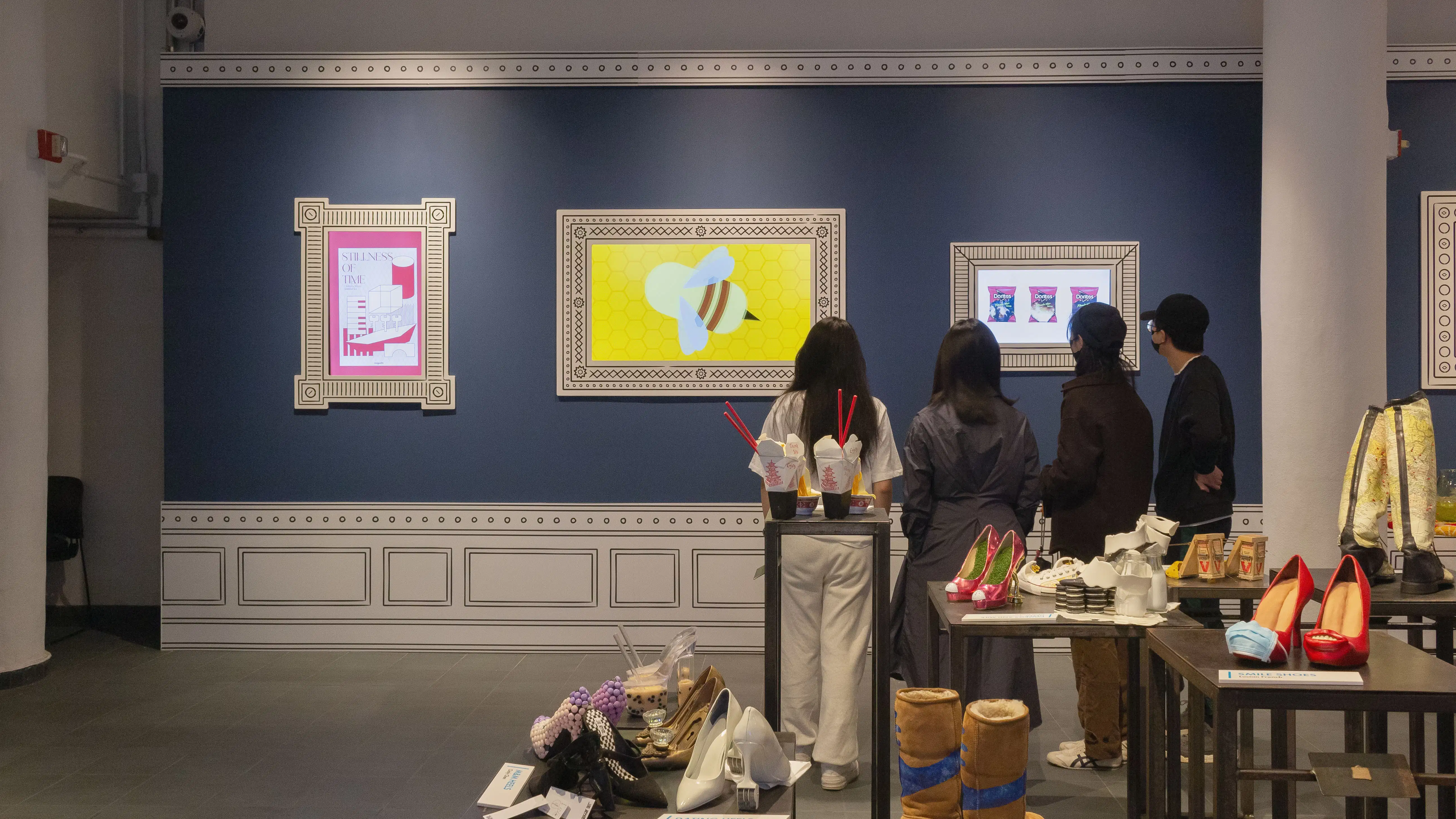 Multiple views of SVA Gramercy Gallery. The lobby is pained red with "Spring Salon" in ornate lettering and the gallery is painted blue. There are monitors in ornate frames playing student work through the gallery. In the center of the lobby and gallery are metal pedestals with student work on them. 