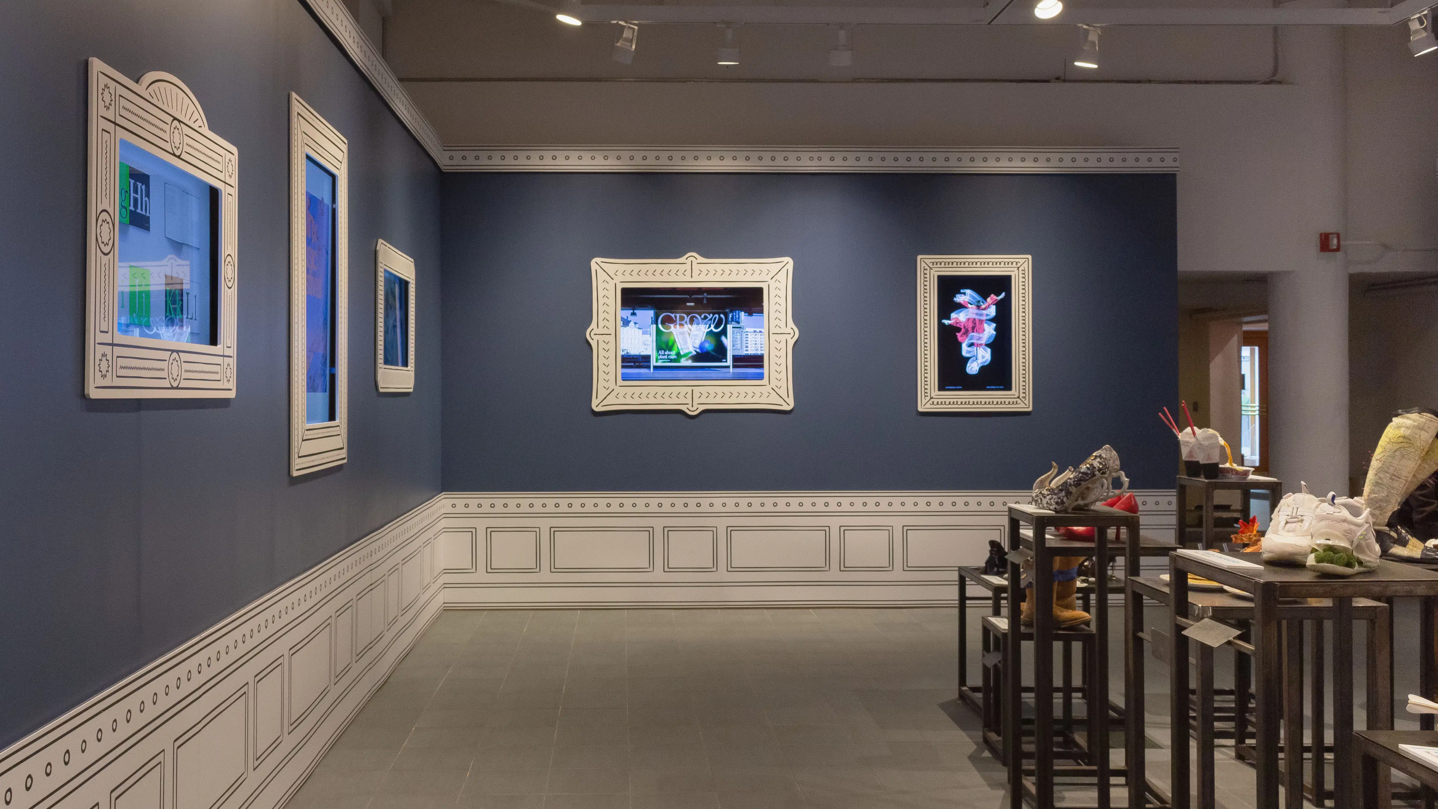 Multiple views of SVA Gramercy Gallery. The lobby is pained red with "Spring Salon" in ornate lettering and the gallery is painted blue. There are monitors in ornate frames playing student work through the gallery. In the center of the lobby and gallery are metal pedestals with student work on them. 