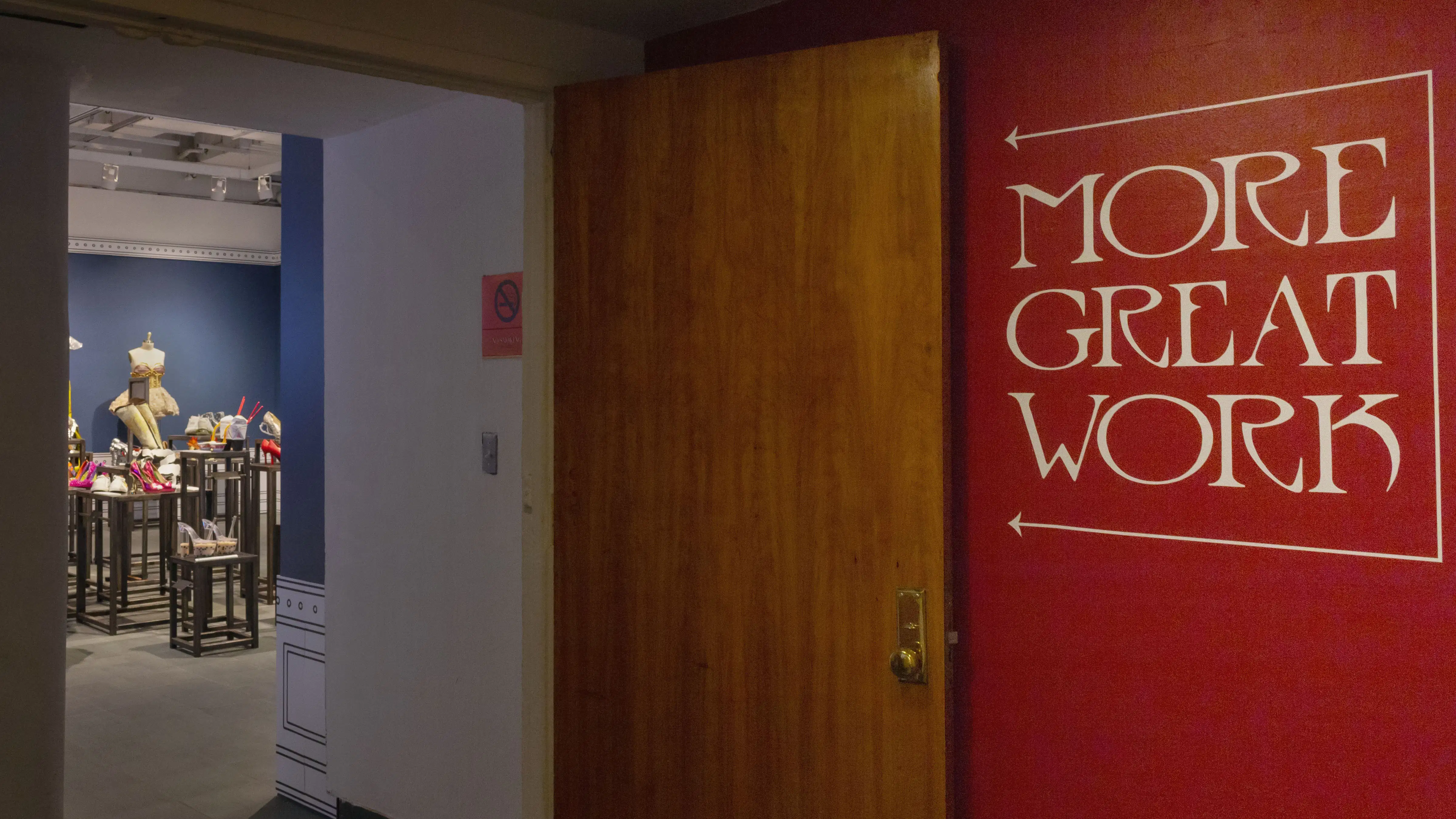 Multiple views of SVA Gramercy Gallery. The lobby is pained red with "Spring Salon" in ornate lettering and the gallery is painted blue. There are monitors in ornate frames playing student work through the gallery. In the center of the lobby and gallery are metal pedestals with student work on them. 
