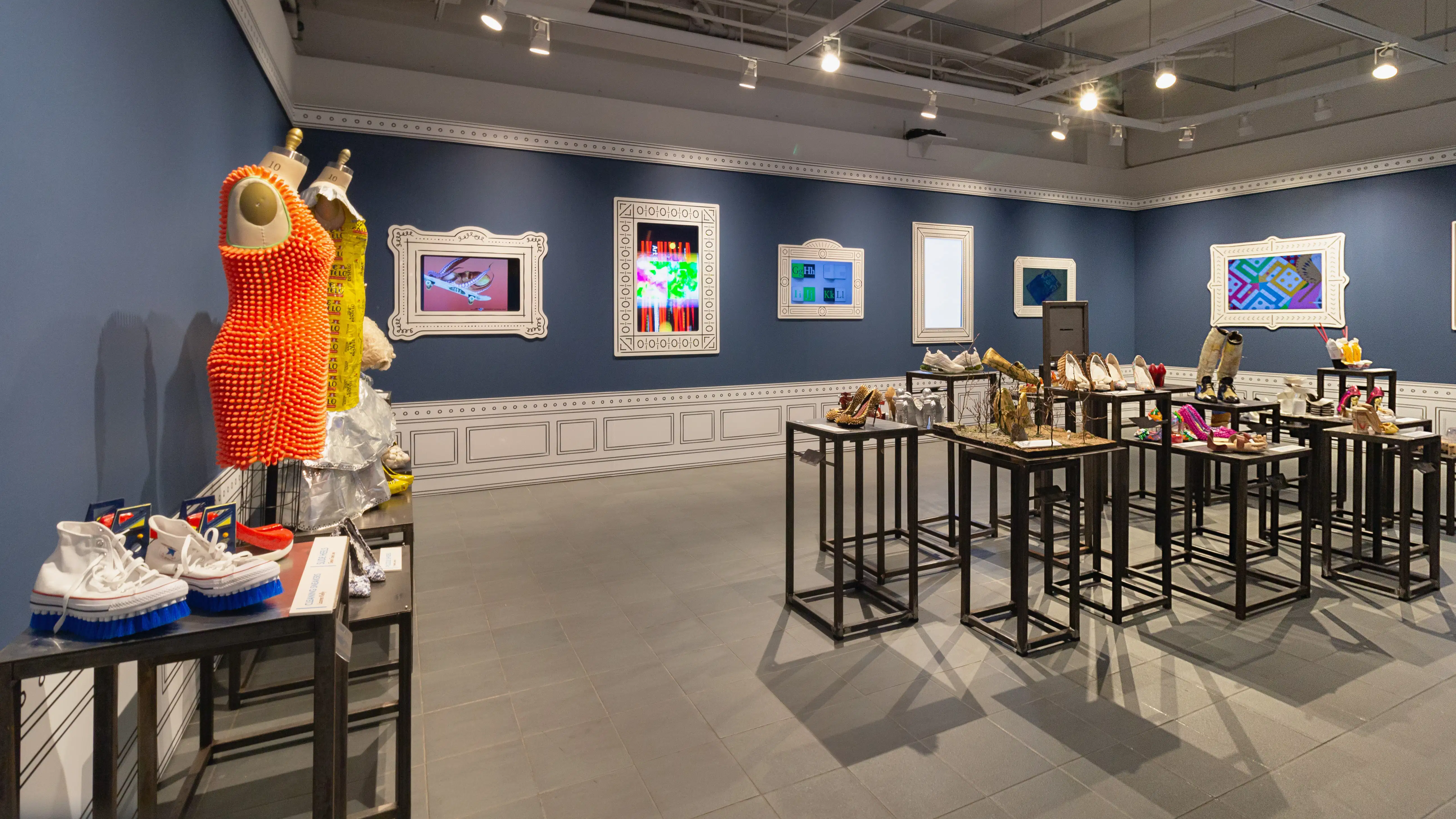 Multiple views of SVA Gramercy Gallery. The lobby is pained red with "Spring Salon" in ornate lettering and the gallery is painted blue. There are monitors in ornate frames playing student work through the gallery. In the center of the lobby and gallery are metal pedestals with student work on them. 