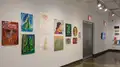 Multiple views of SVA Chelsea Gallery. There is illustrations and paintings hung on the walls. There are multiple shelves throughout the gallery with books places on them.