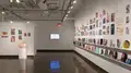 Multiple views of SVA Chelsea Gallery. There is illustrations and paintings hung on the walls. There are multiple shelves throughout the gallery with books places on them.
