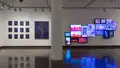 Multiple views of SVA Chelsea Gallery. There are illustrations, monitors, and paintings hung on the walls. Shelves have posters, books, CDs and artist take-aways.