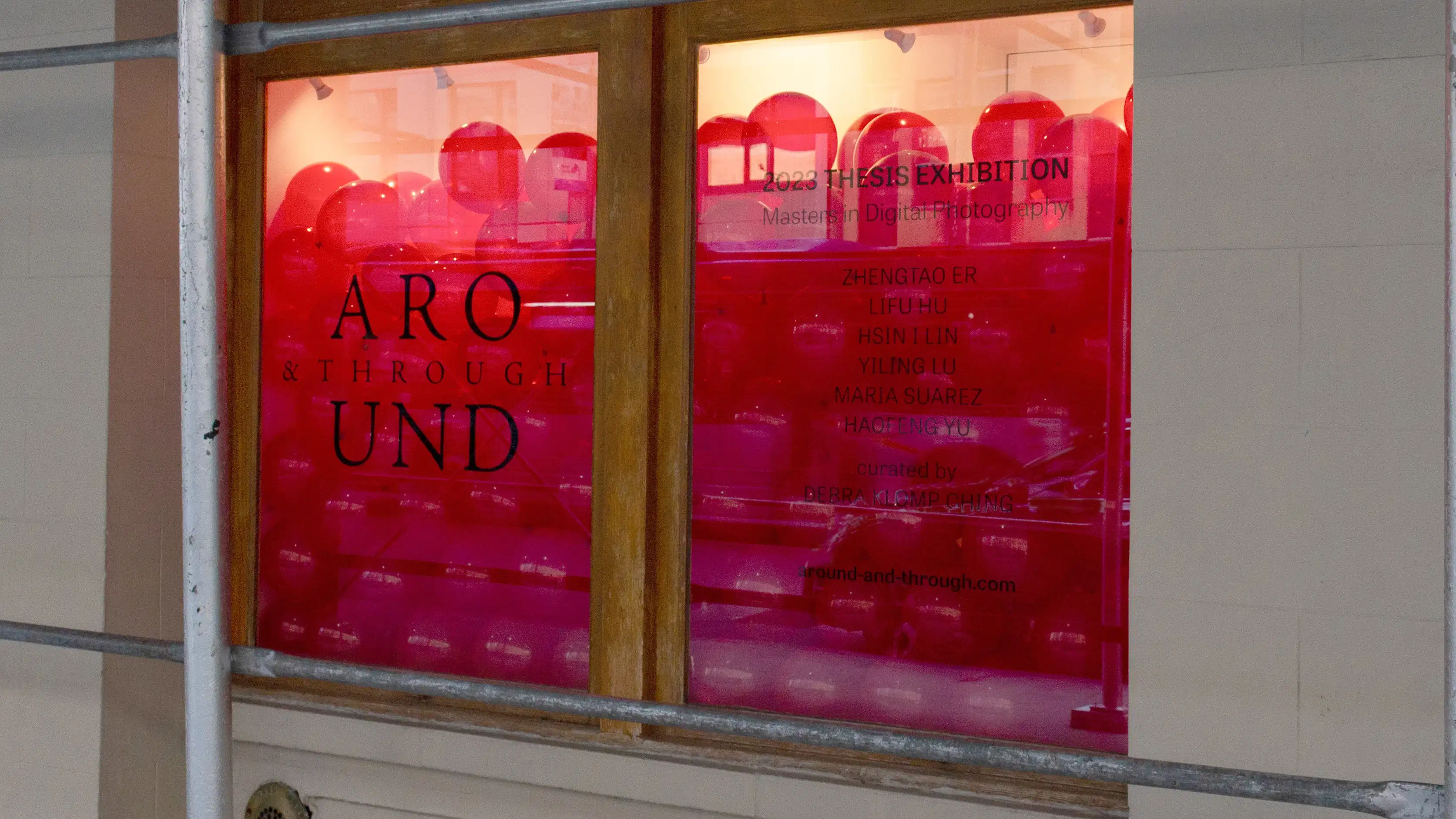 Outside of the SVA Gramercy Gallery, a display window holds a huge pile of red translucent balloons, referencing one of the photographs being shown in the exhibition. Text on the windows displays the exhibition title and artist names.