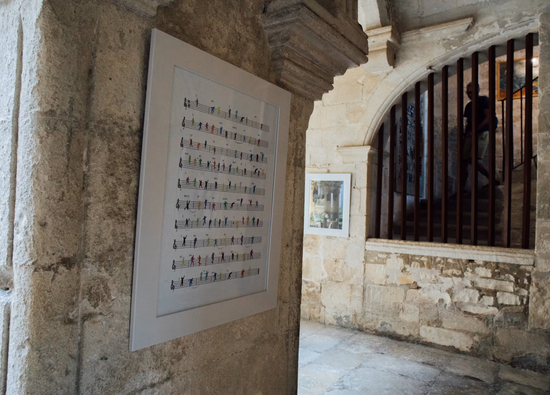 An illustrated work hangs on a corner wall. In the illustration, small figures dance along a sheet of music.