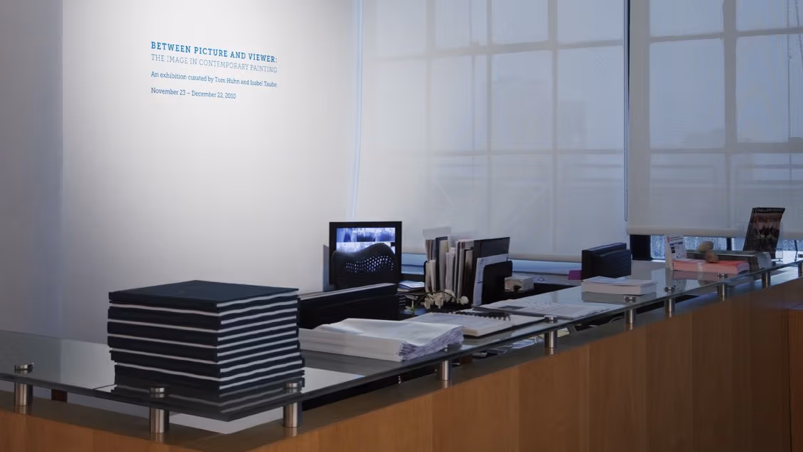 Photograph of front desk at the Visual Arts Gallery, with a stack of catalogs on the left and two computers behind the counter.