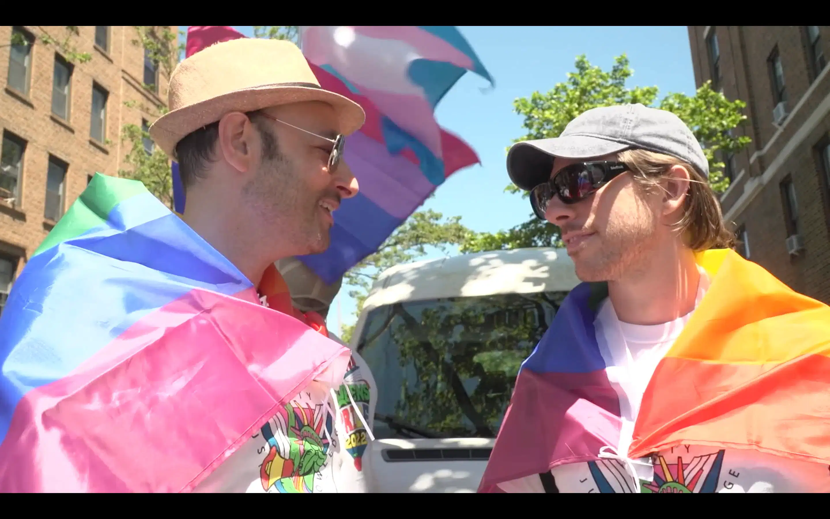 Two men wrapped in pride flags under the sun facing each other 