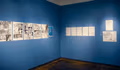 Photograph of two blue walls containing illustrations on paper within gallery space.