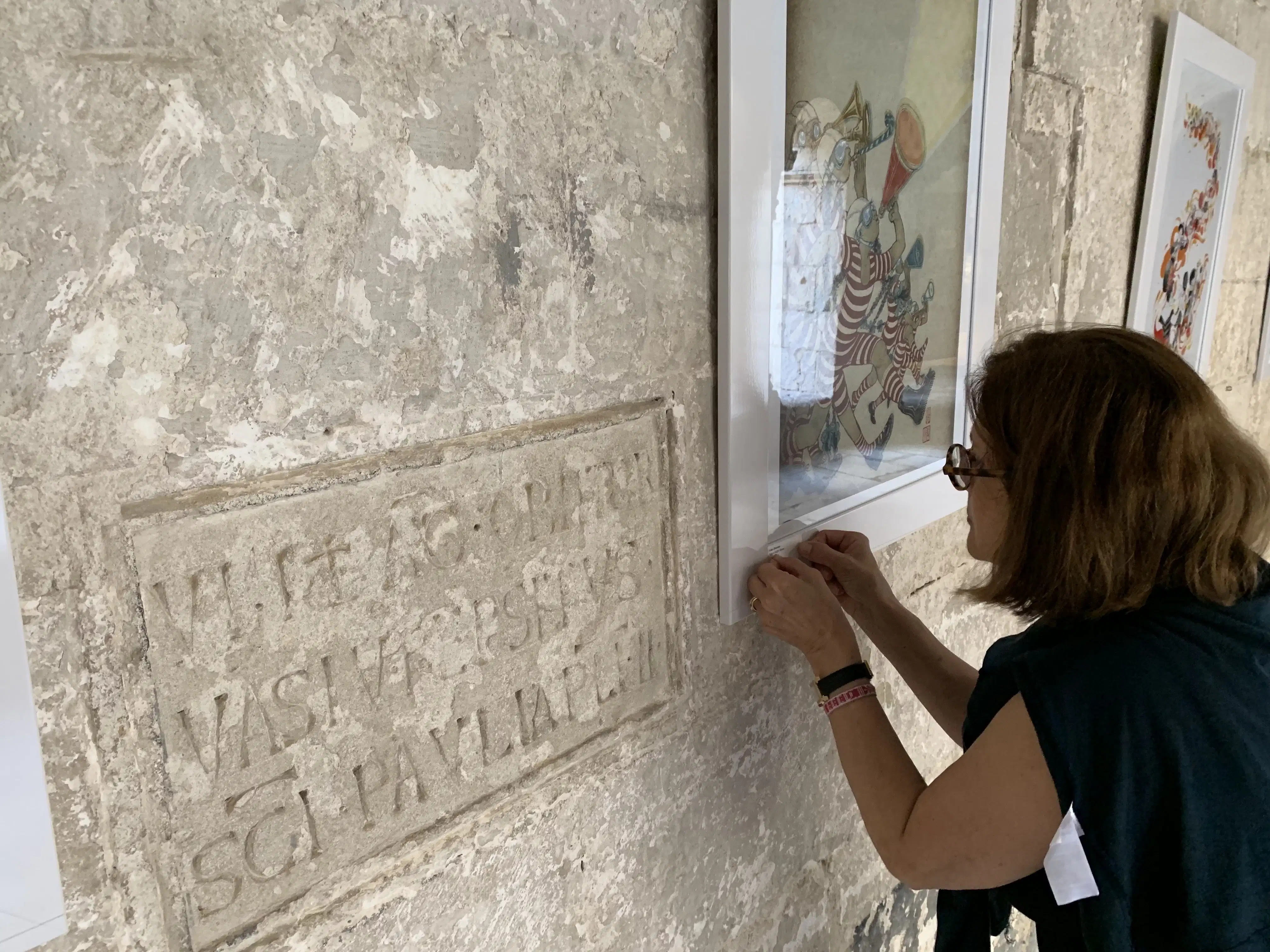 A woman installs a label on one of the framed artworks. Next to the work, lettering is etched into the wall.