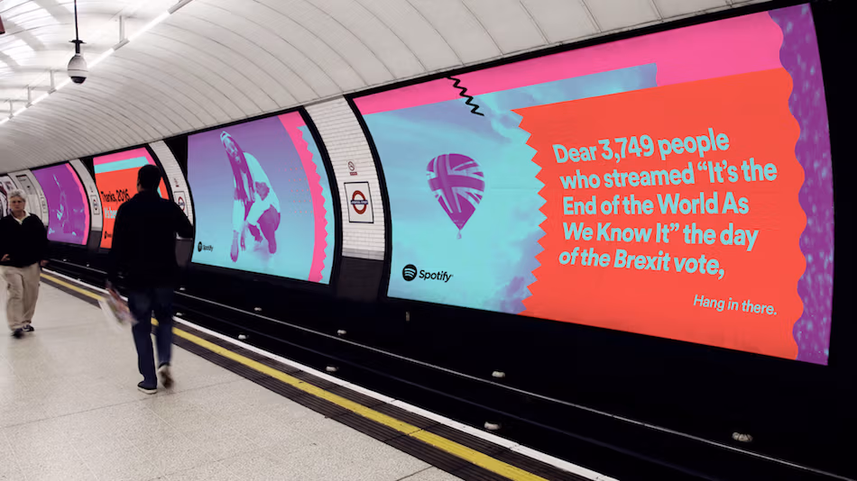 <p "="">A photograph of a London tube station with large colorful ads displayed on the wall.